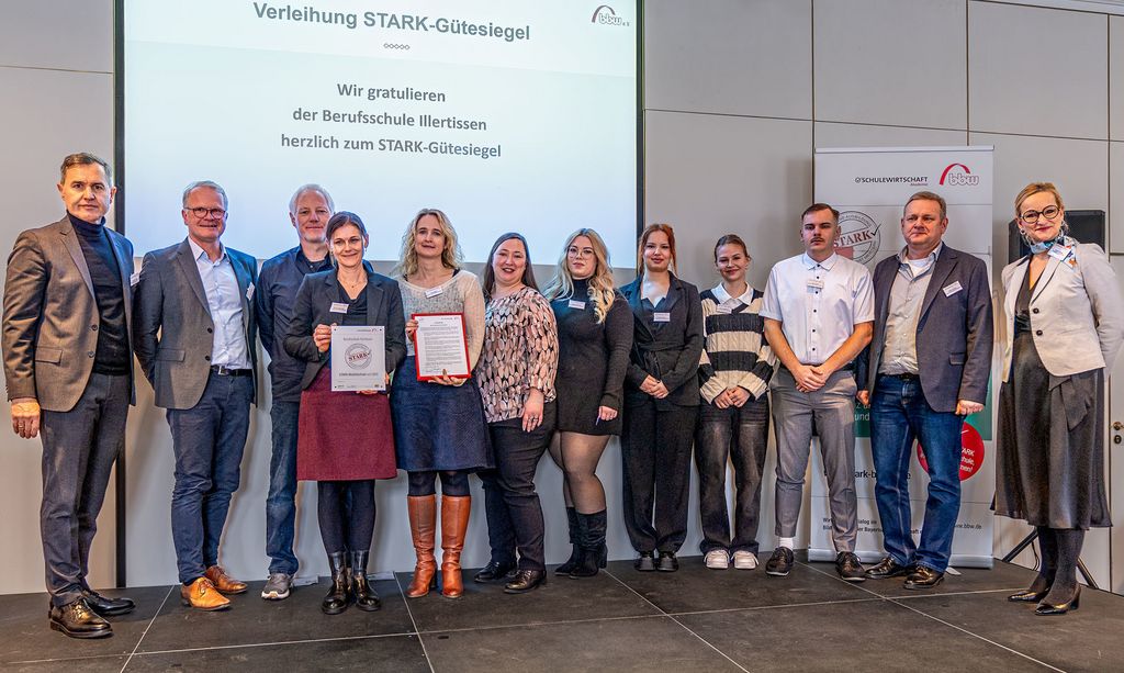 Personengruppe auf Bühne bei der Auszeichnung der Berufsschule Illertissen als STARK-Modellschule, mit Schulleitung, Kollegium, Schülerinnen und Schülern sowie Robert Geiger vom Bayerischen Staatsministerium für Unterricht und Kultus und Sandra Stenger von der bbw-Gruppe.
