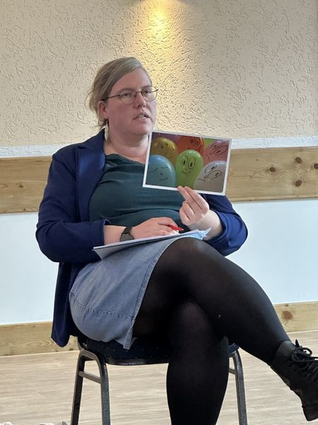 Eine Teilnehmerin hält ein Foto mit bunten, nebeneinander liegenden Luftballons mit aufgemalten Gesichtern hoch und spricht dazu im Workshop.
