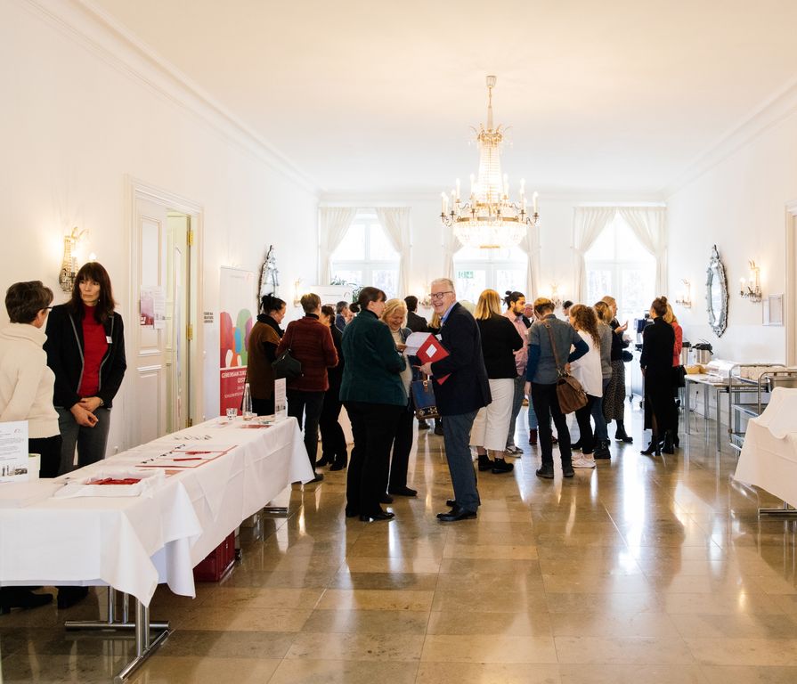 Teilnehmende und Veranstaltende im Austausch im Foyer des Schlosses Fürstenried vor einer STARK-Gütesiegelverleihung.