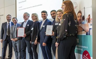 Schulleiter Klaus Weiher sowie Lehrkräfte und Schüler der Berufsschule Neu-Ulm freuen sich auf einer Bühne über das STARK-Gütesiegel; neben ihnen die Laudatoren Martin Wunsch und Florian Kaiser.