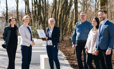 Fünf Personen aus Lehrpersonal und STARK‑Vertretung im Schulhof der FOS Haar; ein Mann hält eine gerahmte Laudatio, eine Frau ein Acryl‑Gütesiegel zur Auszeichnung als STARK‑Modellschule 2021